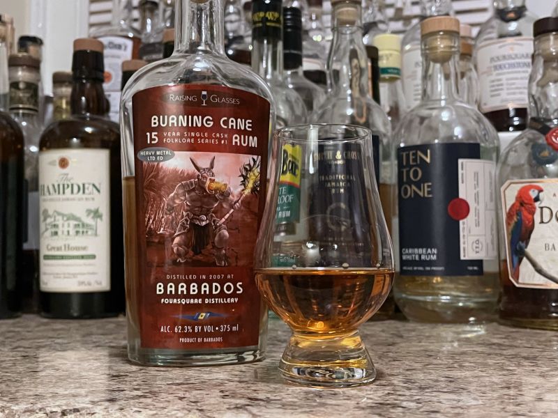 Raising Glasses Burning Cane bottle next to a glass of rum