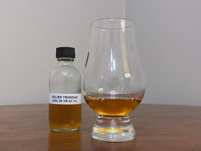 A bottle of La Maison & Velier Flag Series Trinidad next to a glass of rum on a tabletop