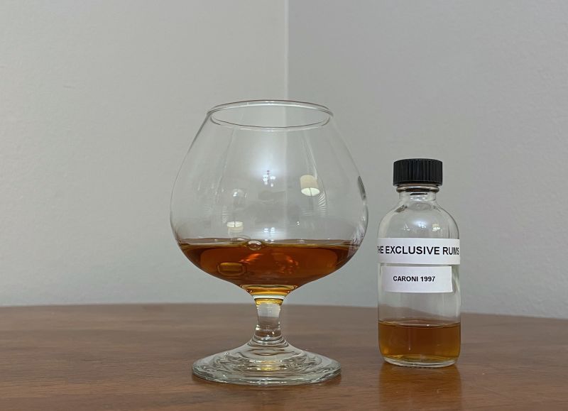 Sample bottle of The Exclusive Rums Caroni 1997 next to a glass of rum