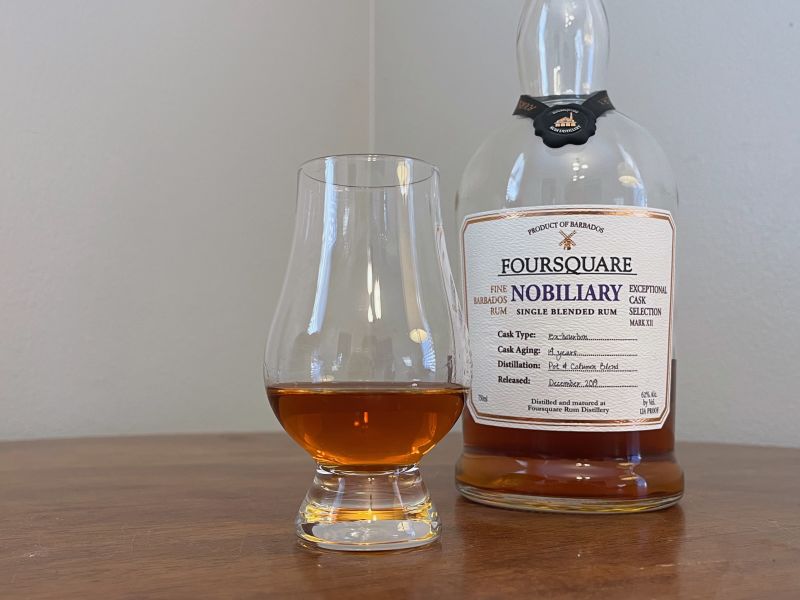 A bottle of Foursquare Nobiliary next to a glencairn of rum on a table