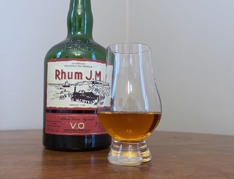 Bottle of Rhum JM VO next to a glencairn of rum on a table