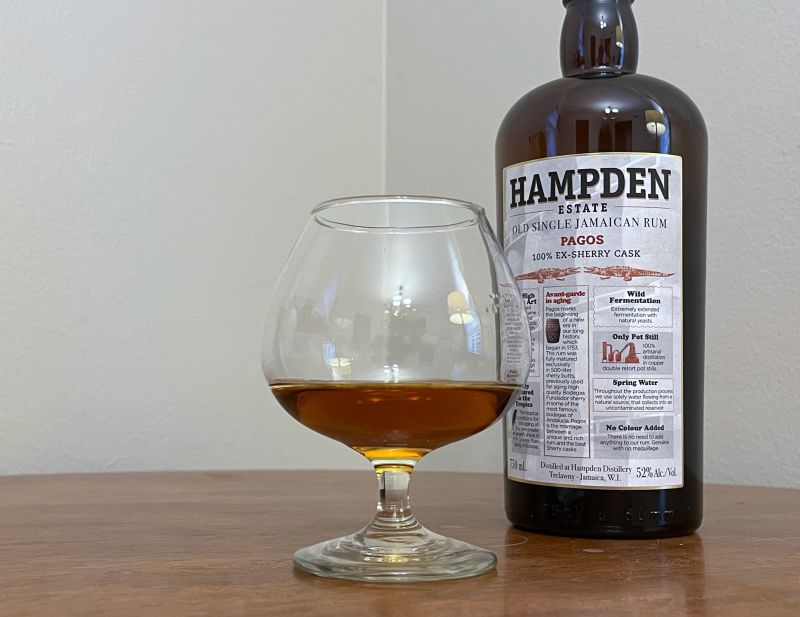 A bottle of Hampden Pagos next to a glencairn of rum on a table