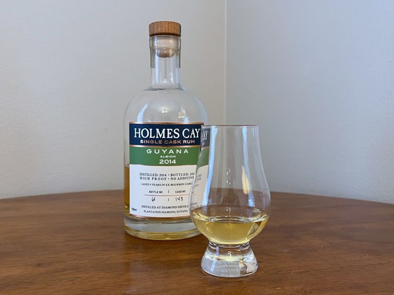 Bottle of Holmes Cay Guyana rum on a tabletop next to a Glencairn of rum