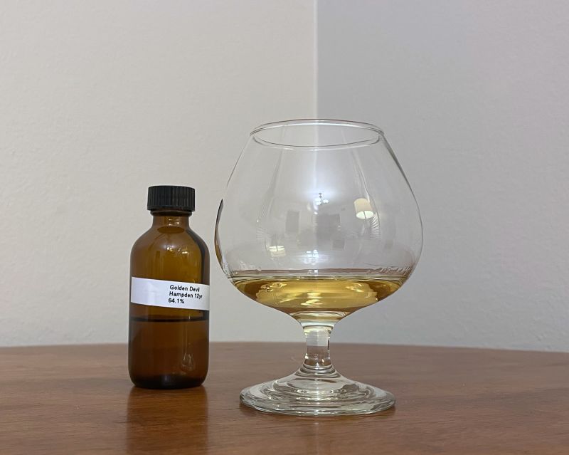 A sample bottle of Golden Devil Jamaica 2007 next to a glass of rum