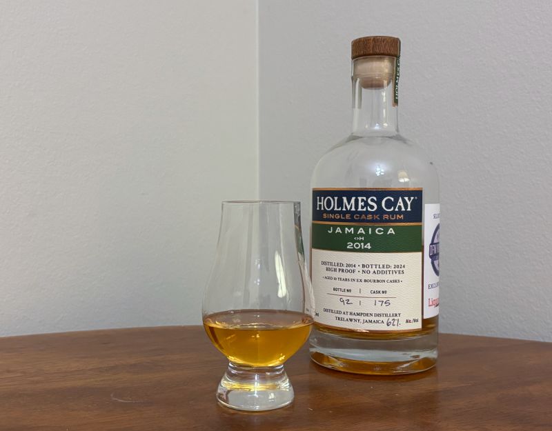 A bottle of Holmes Cay Jamaica <>H 2014 10 year next to a glass of rum