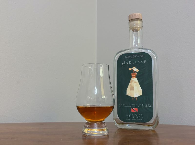A bottle of Raising Glasses Jablesse Trinidad 21 year next to a glass of rum
