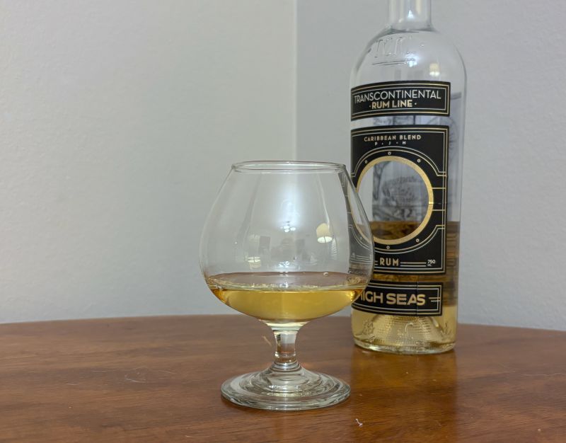 A bottle of Transcontinental Rum Line High Seas next to a glass of rum