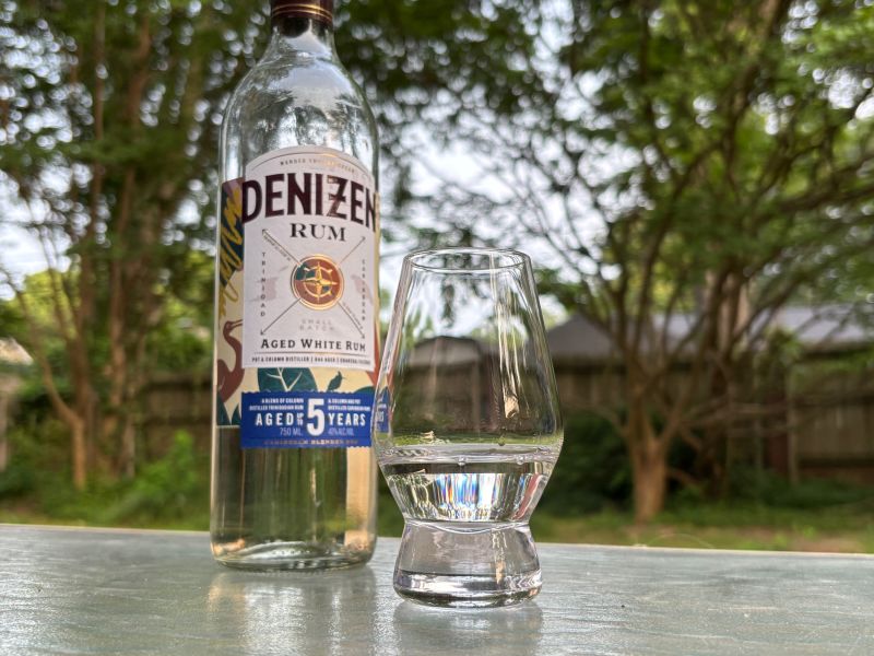 A bottle of Denizen Aged White Rum next to a glass of rum