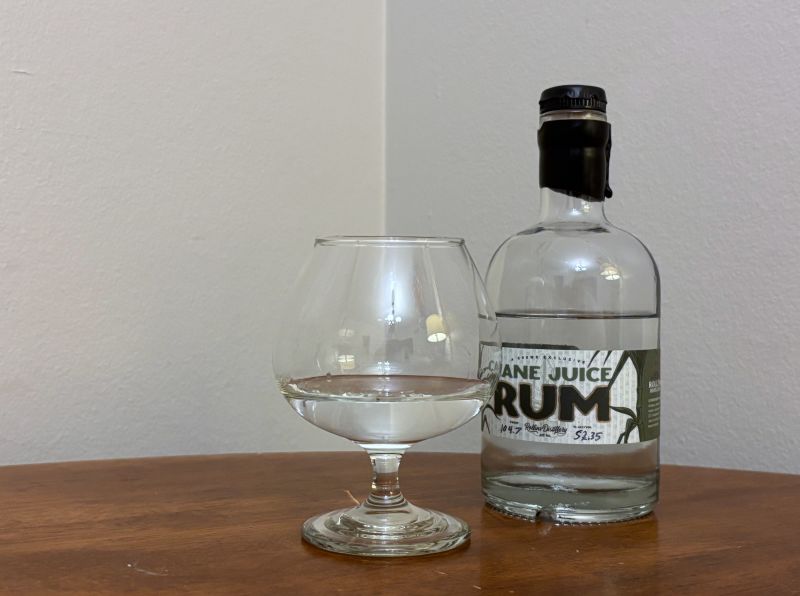 A bottle of Krewe Exclusive Cane Juice Rum next to a glass of rum