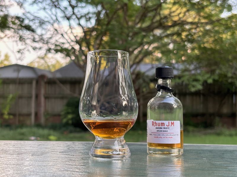 A bottle of Rhum JM Atelier Series Jardin Fruité  next to a glass of rum