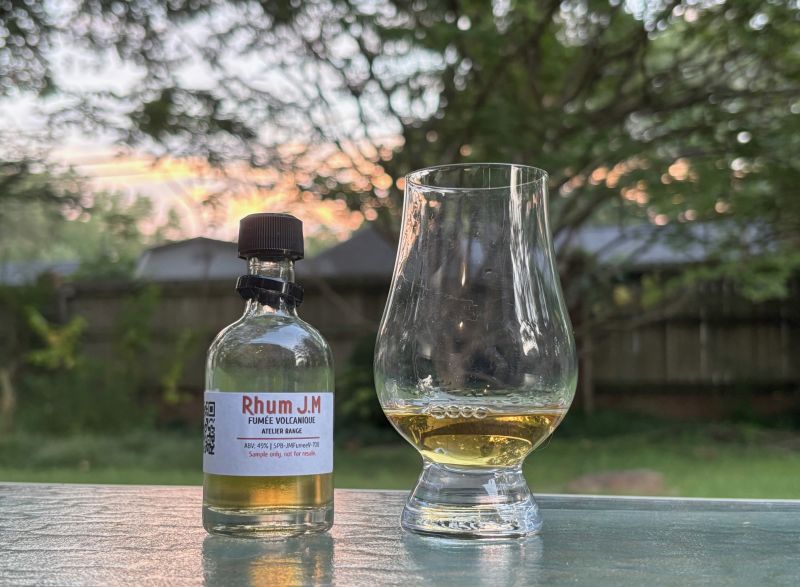 A bottle of Rhum JM Atelier Series Fumée Volcanique next to a glass of rum