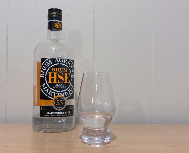 A bottle of Rhum HSE Blanc Agricole 55º next to a glass of rum
