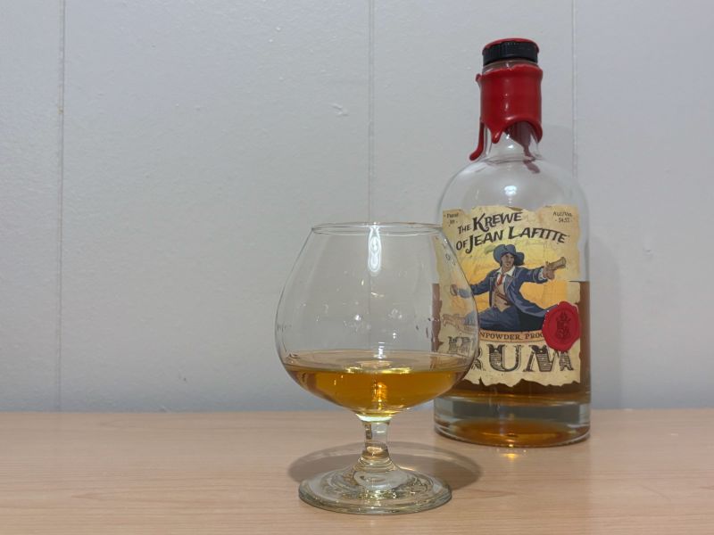 A bottle of Krewe of Jean Lafitte Gunpowder Proof next to a glass of rum