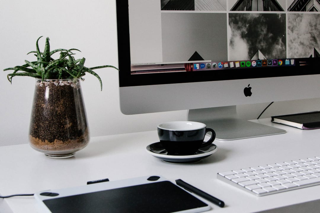 minimal desk setup for a designer featuring iMac, succulent plant, Wacom graphics tablet, and coffee cup.