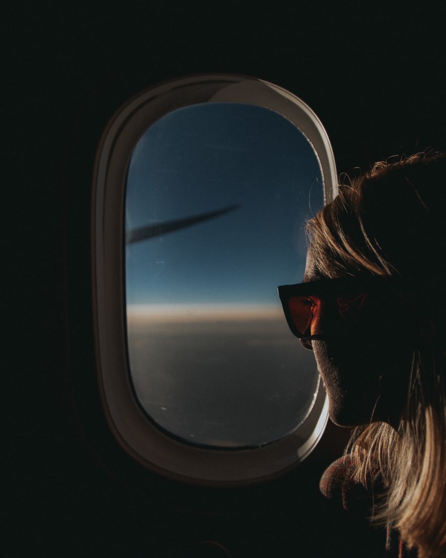 Girl looking out of plane window at sunset wearing Tens sunglasses