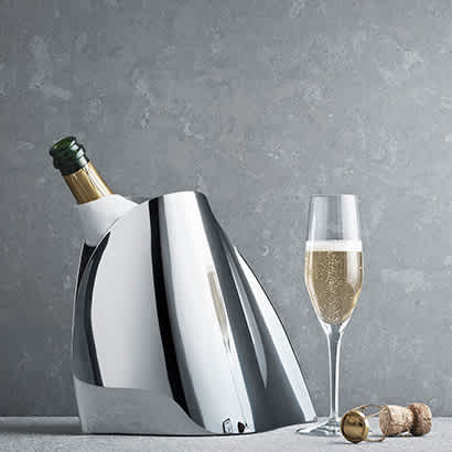 champagne cooler in Mirror polished stainless steel with bottle inside and glass next to it from the Indulgence collection designed by Helle Damkjær for Georg Jensen