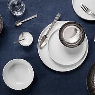 Borddækning med skåle og tallerkener i hvidt porcelæn samt klassisk bestik og skåle i stål fra Bernadotte kollektionen inspireret af Sigvard Bernadottes klassiske designs