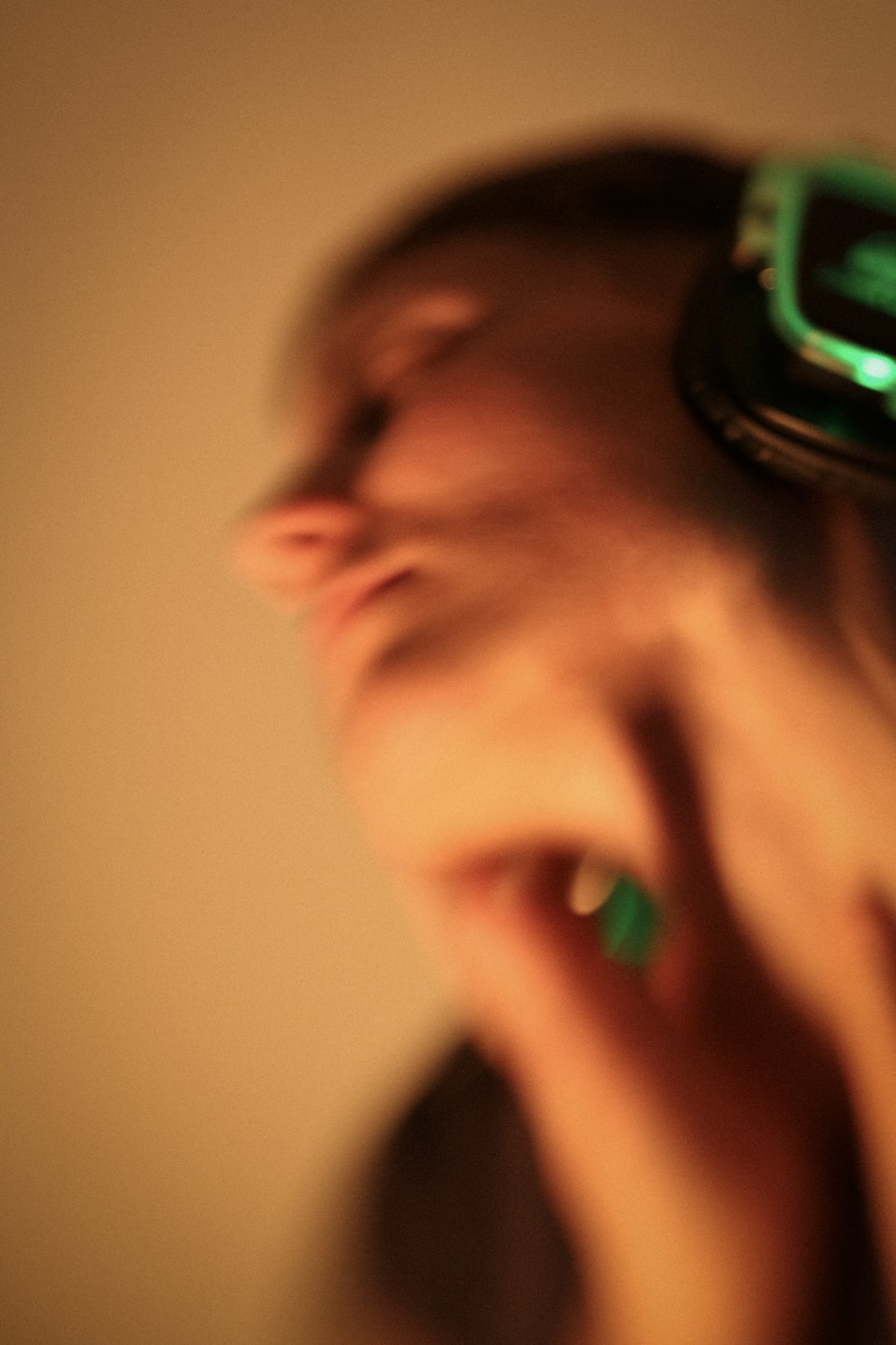 Unscharfes Bild einer tanzenden Person, deren Gesicht verschwommen ist. Sie trägt Kopfhörer, die grün leuchten.