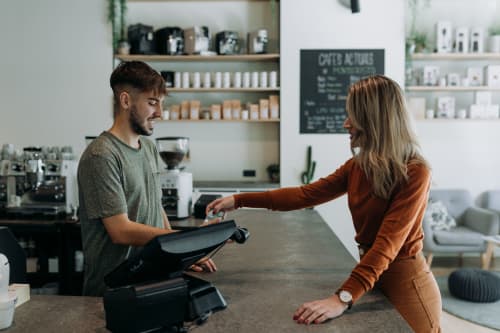 Woman making a purchase from male cashier in coffee shop