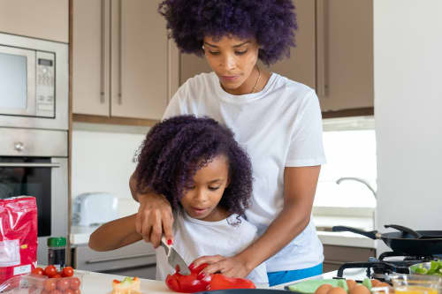 mom helping young daughter cut bell pepper