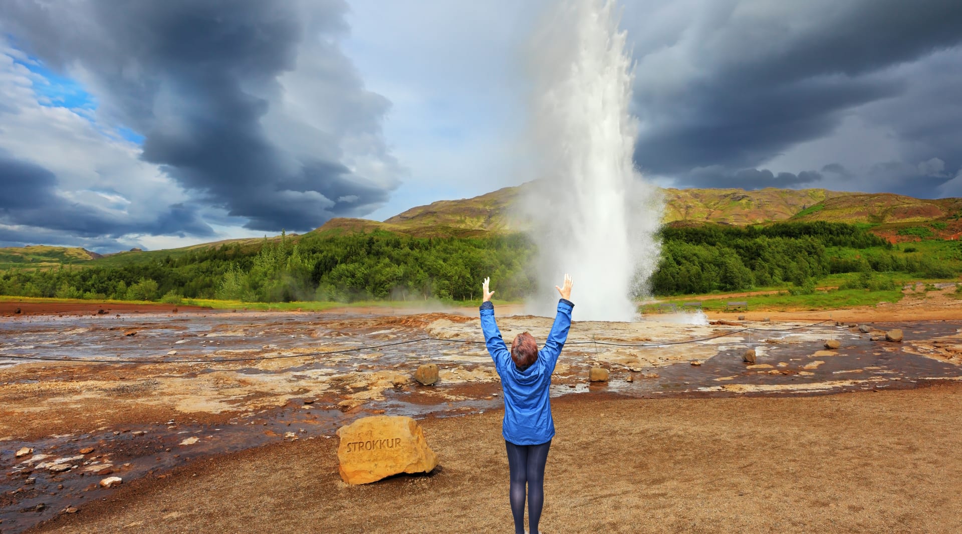 Geysir erupting with happy woman in front