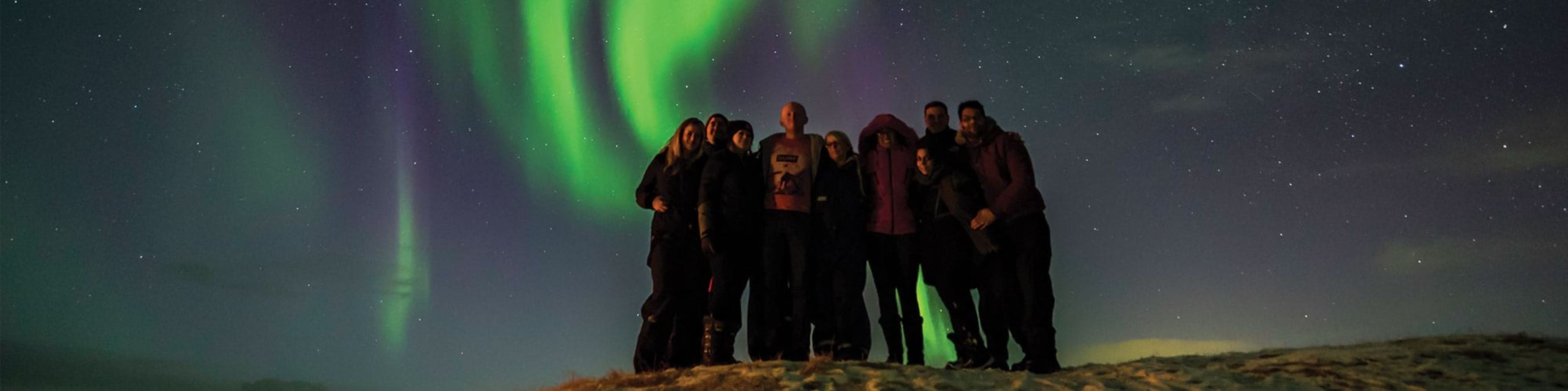 Peaple posing with northern lights in the background at night