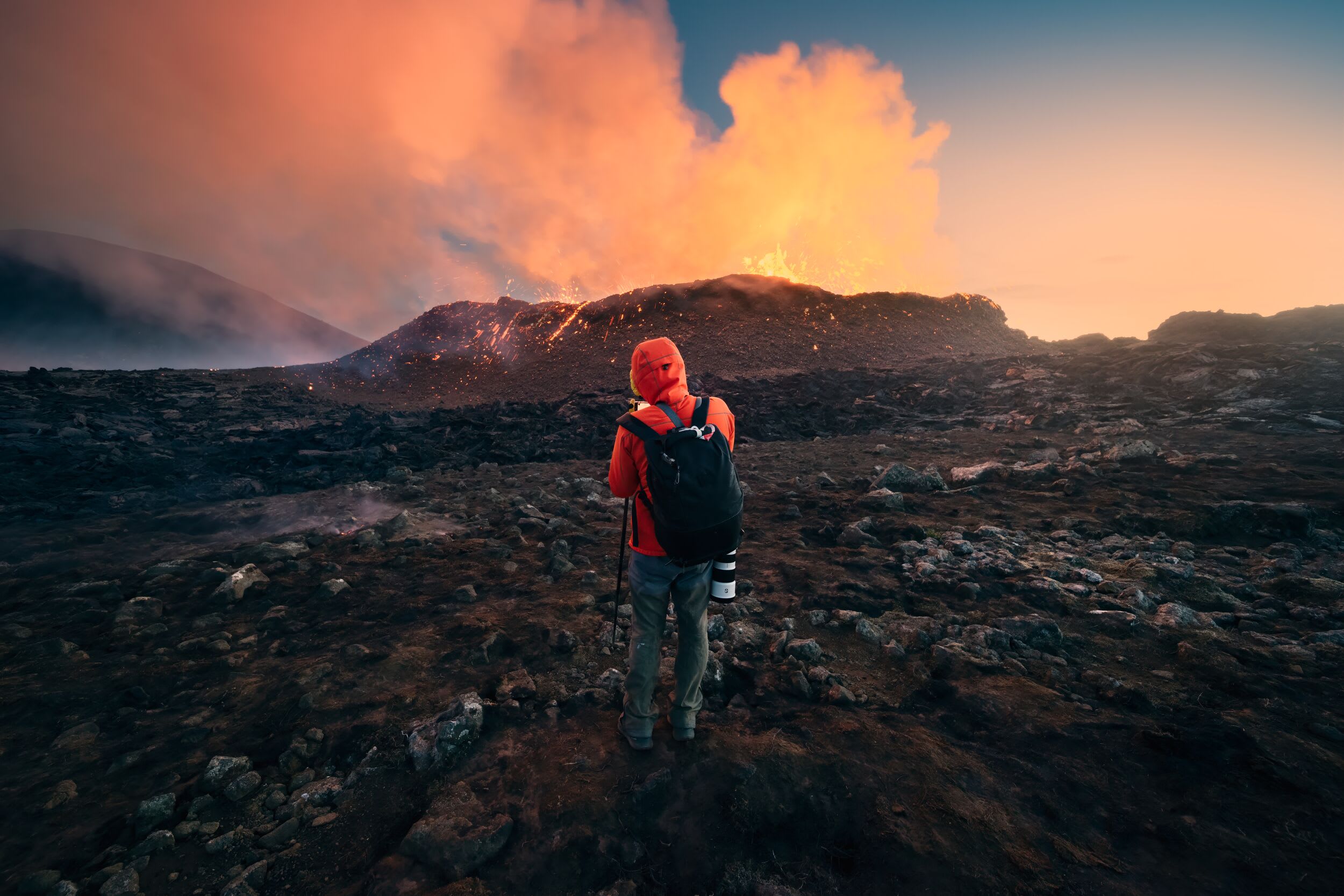 A solo traveler looking at the sunrise behind an active eruption in Fagradalsfjall