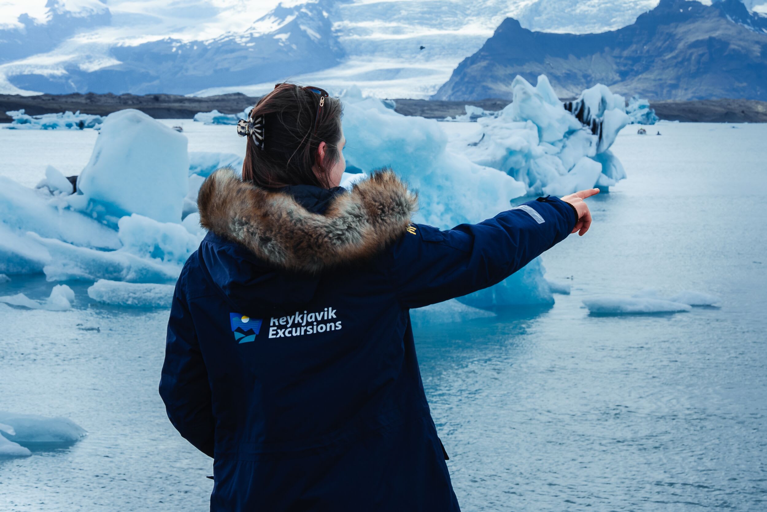 A guide at Jökulsárlón Glacier lagoon pointing out at the water in a branded coat