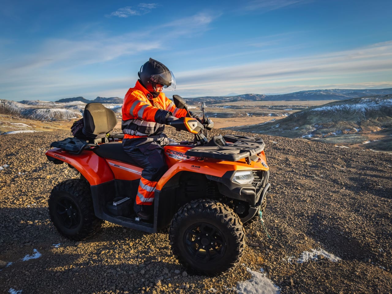 A person on a ATV on top of a mountain in Iceland with a blue sky in the background in spring with some snow sprinkled on surrounding mountains