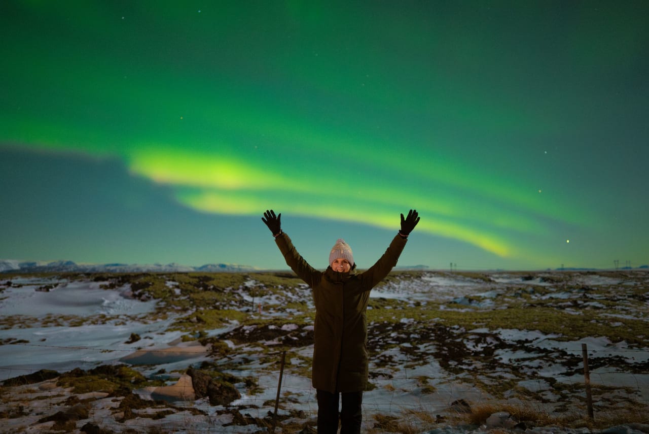 A women standing under the northern lights on a cold dark evening in Iceland