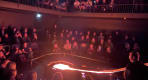 Thumbnail about Smiling audience members sit close to a steaming lava pit, lit in red and white as molten rock cools and releases steam.