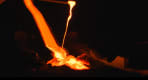 Thumbnail about Molten lava flows in bright orange from a tilted container into a cooling pit, glowing intensely against a dark background.