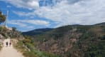 Thumbnail about Hikers walking along a dirt trail on the Paiva Walkways with the Arouca 516 suspension bridge crossing the valley in the background.