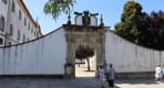 Thumbnail about Stone arch entrance to Arouca Monastery with visitors standing outside in Portugal.