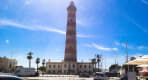 Thumbnail about Barra Lighthouse near Aveiro with striped tower, palm trees, cars, and blue sky