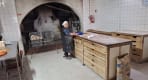 Thumbnail about Favaios bakery kitchen with baker beside wooden worktables, bread crates, tiled walls, and traditional oven