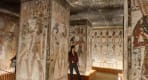 Thumbnail about A visitor standing inside a lit chamber with painted stone pillars and colorful ancient hieroglyphic reliefs 