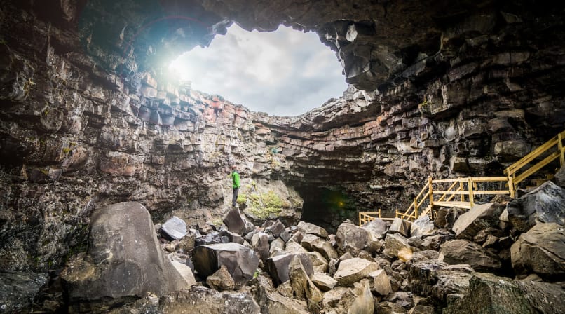 A guide stands atop a large basalt boulder, giving a sense of the vastness of Víðgelmir.