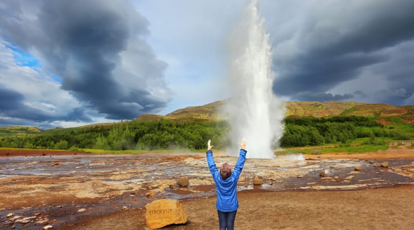 Geysir erupting with happy woman in front