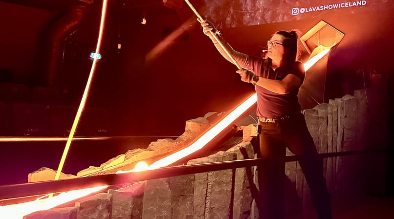 An overhead view of an audience seated around a lava channel in a dark theater, watching the glowing lava flow through the stage.