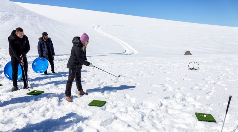person playing golf ontop the glacier, standing in white snow