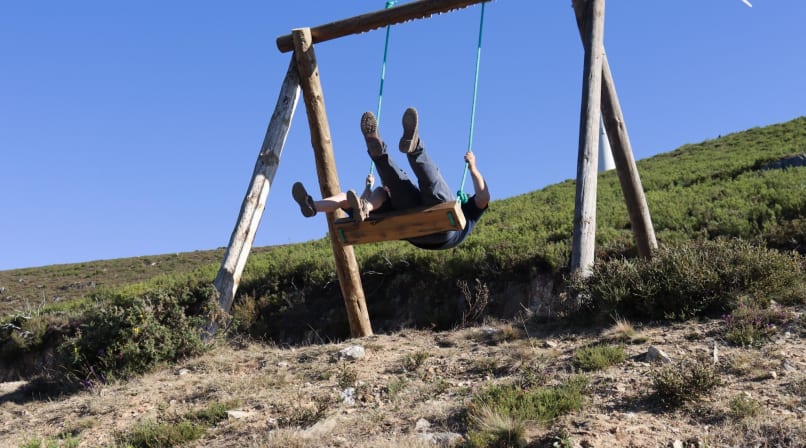 Person swinging on a wooden swing overlooking a mountain landscape