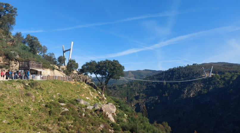 View of the Arouca 516 suspension bridge crossing a deep valley in Portugal, with visitors near the entrance and mountains in the background