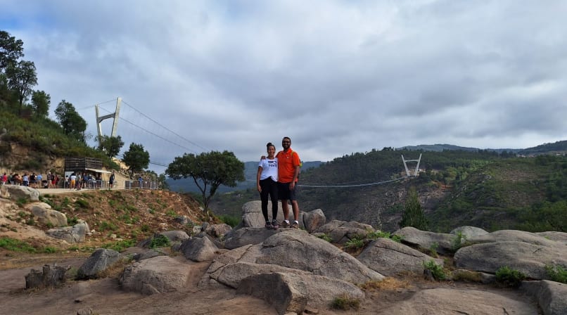 Couple standing on rocks overlooking the Paiva valley with the Arouca 516 suspension bridge in the background.