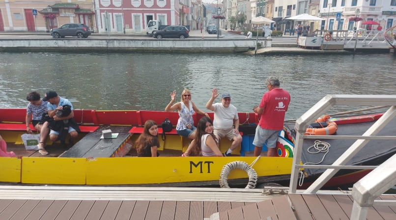 Guests waving from yellow moliceiro boat on Aveiro canal beside boarding dock