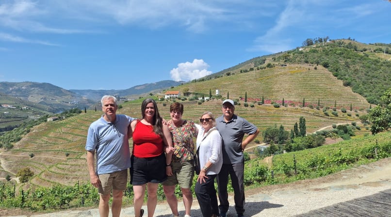 Group posing at Quinta do Seixo viewpoint with Douro Valley terraced vineyards, hills, and blue sky behind