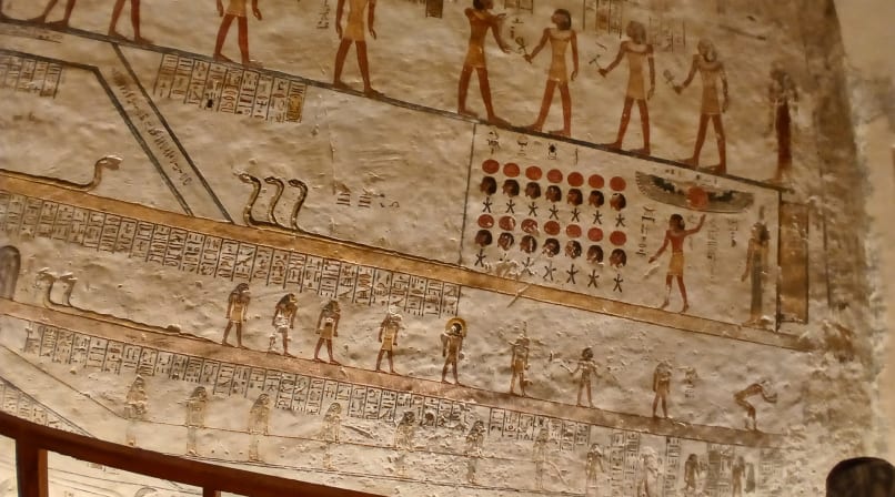 A close-up view of a beige stone wall with colorful, finely carved Ancient Egyptian hieroglyphs and deities inside the tomb of Merenptah