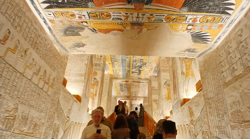 Tourists walking along a wooden path under a yellow-painted ceiling depicting the goddess Nut