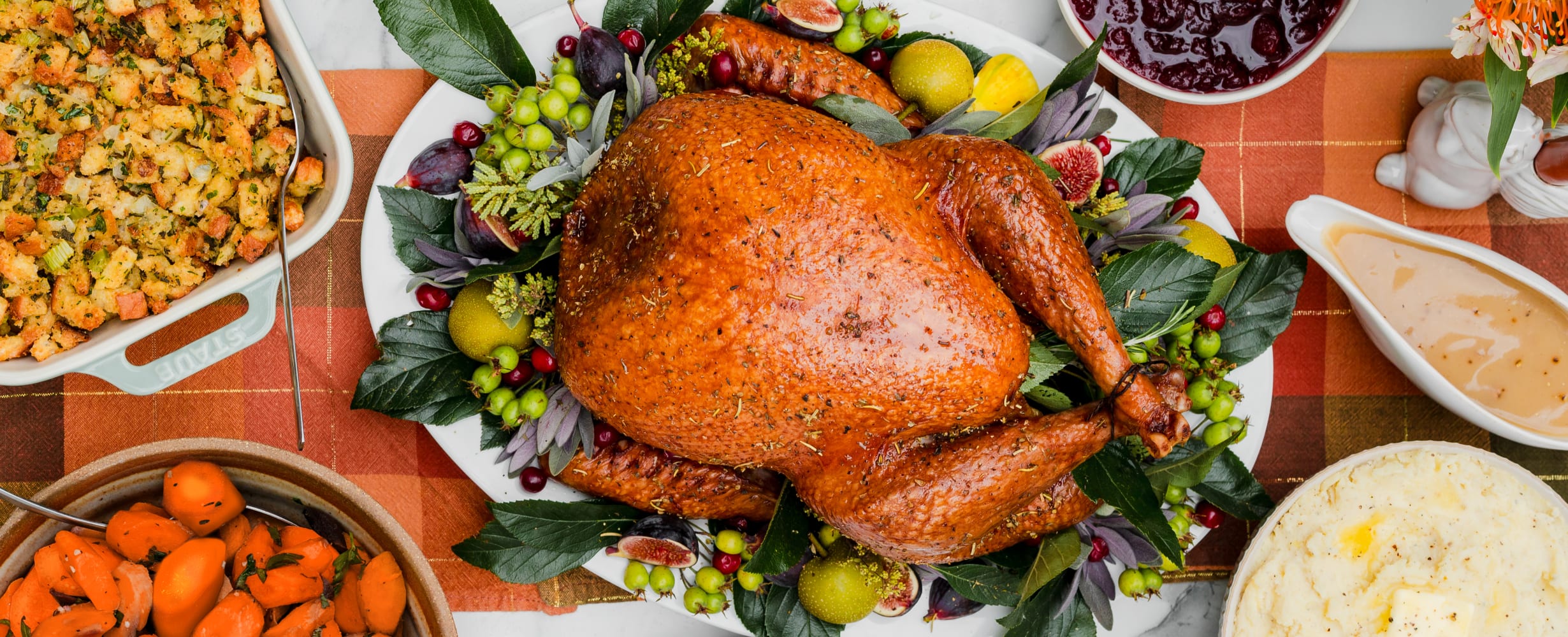 An image of a cooked turkey surrounded by sides like carrots, mashed potatoes, gravy, cranberry sauce, and stuffing.