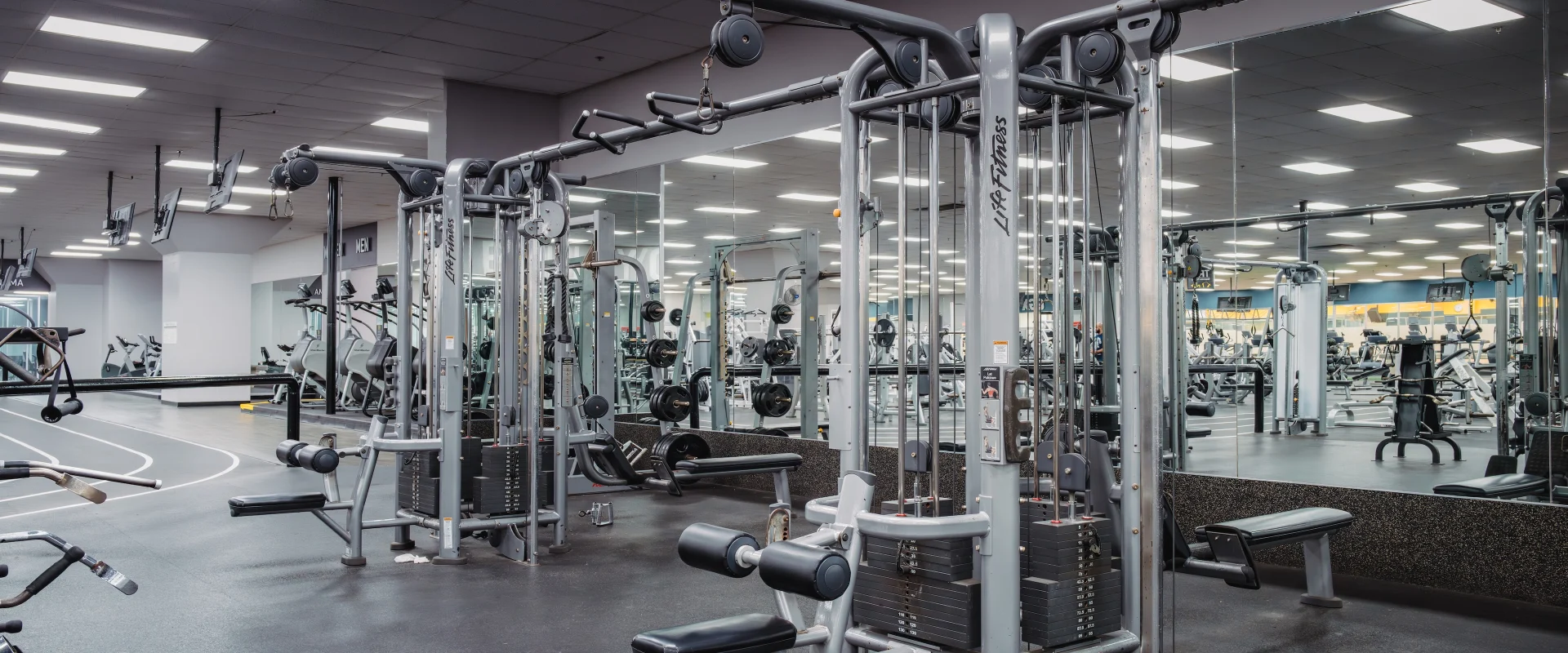 Resistance machines at Gold’s Gym in Austin (South Central), featuring Life Fitness cable machines with adjustable pulleys for versatile strength training. The area includes padded benches and a variety of attachments for targeting different muscle groups. Mirrored walls enhance visibility, while rubber flooring and bright overhead lighting create a clean, organized workout environment.